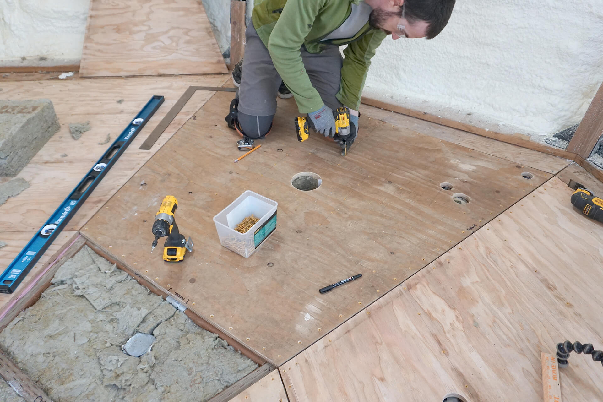 Installing the plywood subfloor over the insulated floor joists.